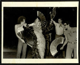 Photograph of a performer posing surrounded by folding fans. 