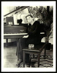 Photograph of Janet MacHarg sitting at her piano waving a cigarette. 