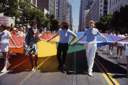 A group of people carrying a large rainbow flag in the International Lesbian & Gay Freedom Day Parade.