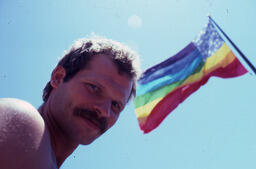 A man photographed with the Lynn Segerblom rainbow flag at 1978 San Francisco Pride.