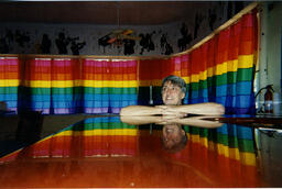 A snapshot portrait of Gilbert Baker in front of a row of rainbow-curtained windows.