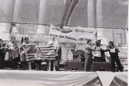 An image of the main stage presentation by Bay Area American Indian Two Spirits (BAAITS) at the 2008 San Francisco Pride festival. Some members are carrying an American flag containing the phrases "Free Leonard Peltier" and "Free all political prisoners." Leonard Peltier is a Native American activist whose incarceration remains controversial. 
