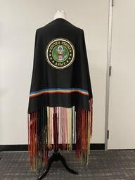 A shawl owned by a member of Bay Area American Indian Two Spirits (BAAITS). It has the United States Army crest on it and rainbow tassels around each edge. 
